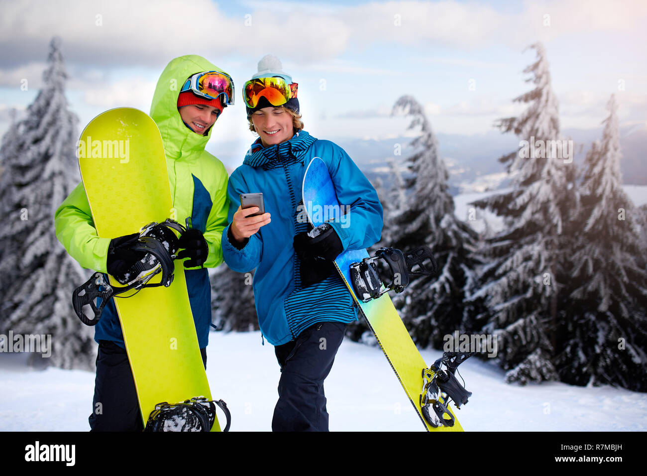 Due gli snowboarder parlando e tenendo gli smartphone. Amici guardando il cellulare e di comunicare nella rete sociale a condividere le loro foto in app con connessione internet indossando variopinti outfit moda. Foto Stock