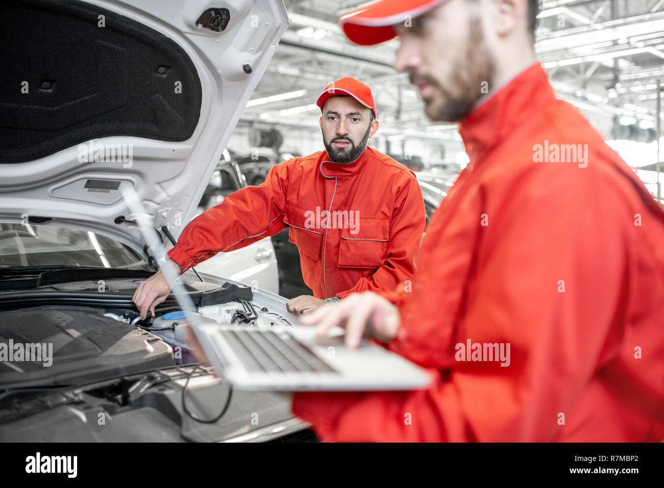 Due auto meccanica in rosso uniforme facendo la diagnostica motore con il calcolatore in auto di servizio Foto Stock