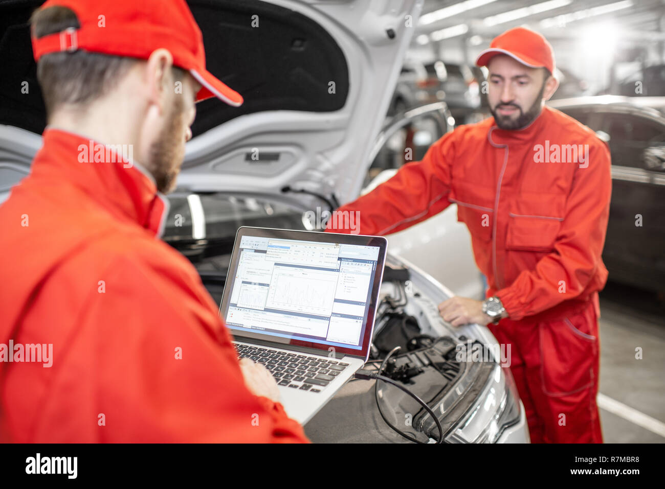 Due auto meccanica in rosso uniforme facendo la diagnostica motore con il calcolatore in auto di servizio Foto Stock