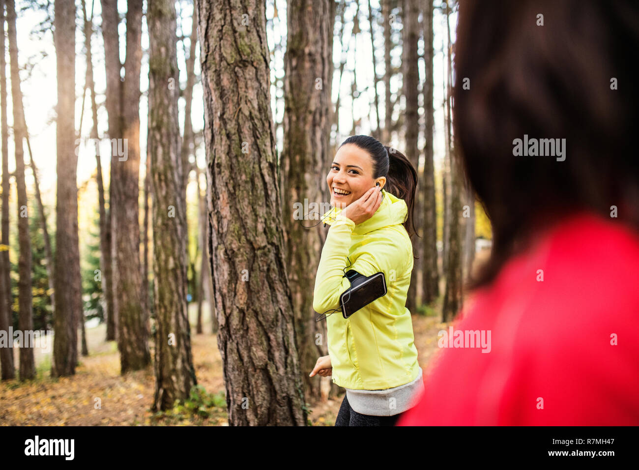 Femminile con gli auricolari e smartphone jogging all'aperto nella foresta. Foto Stock