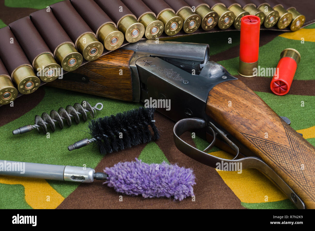 Fucile da caccia e munizioni con spazzole per la pulizia di armi giacenti su un camuffamento di sfondo. Foto Stock