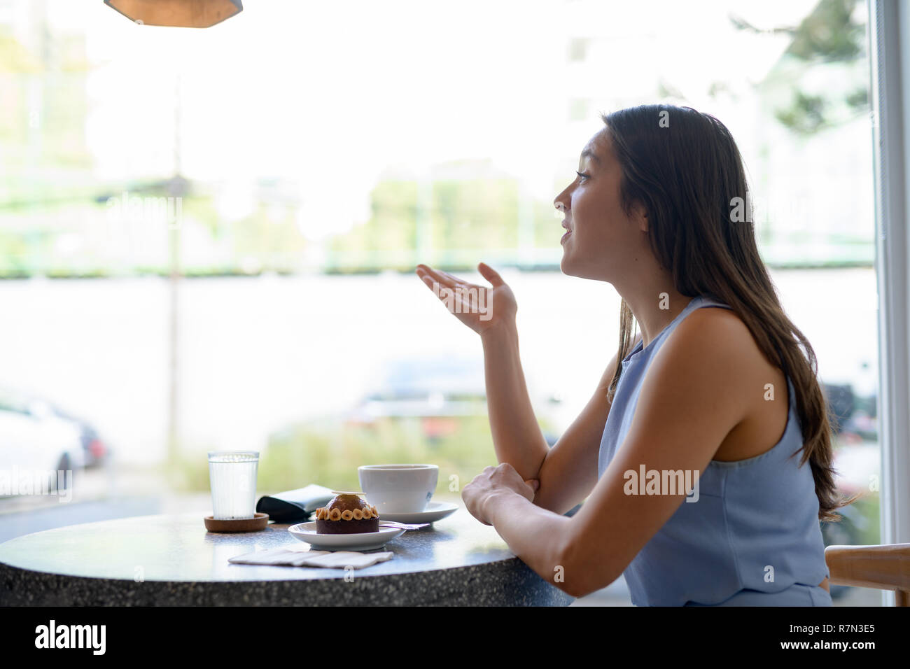 Vista di profilo del giovane bella imprenditrice parlando dalla finestra al coffee shop Foto Stock