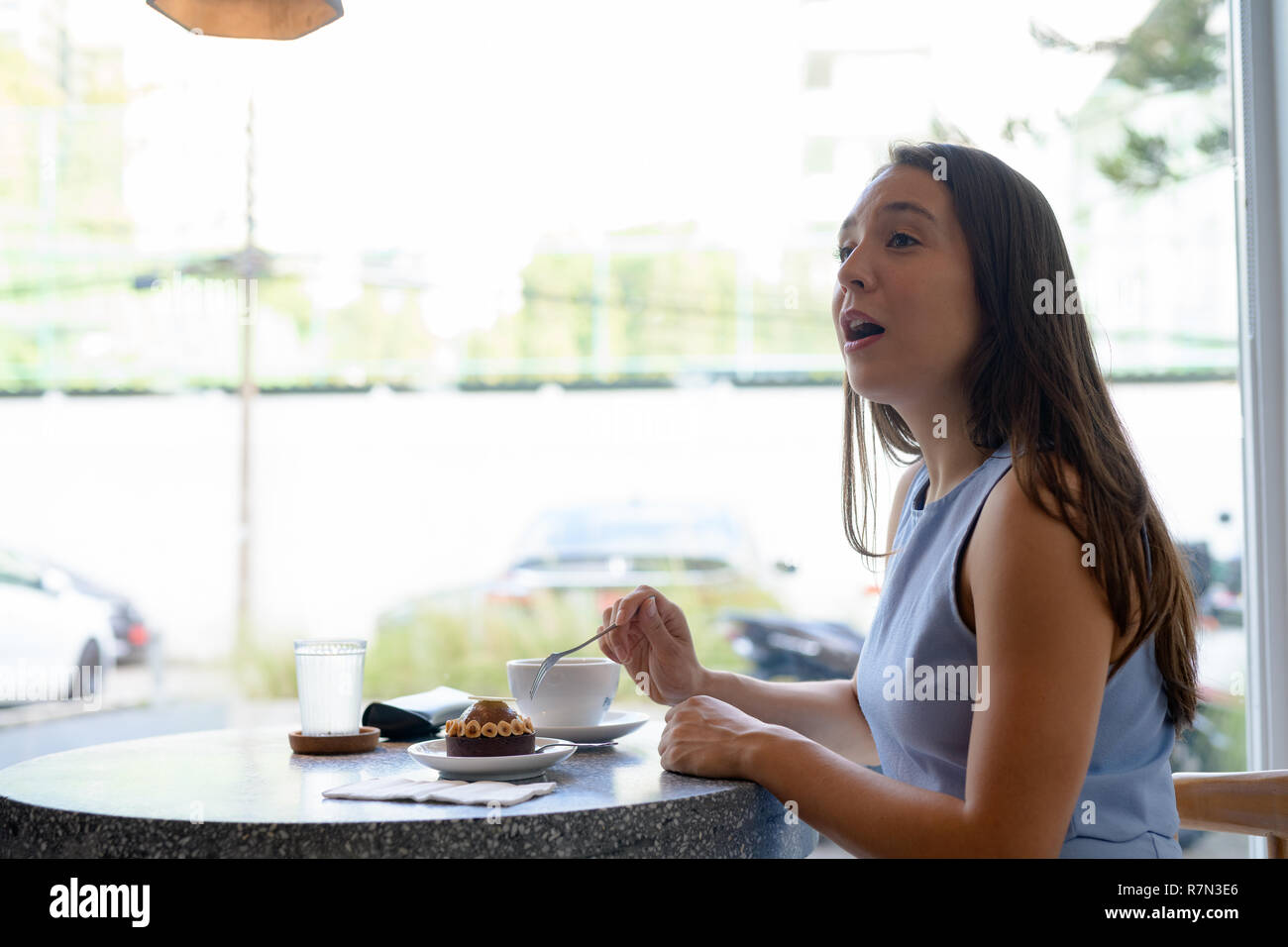 Vista di profilo del giovane bella imprenditrice di mangiare la torta dalla finestra Foto Stock