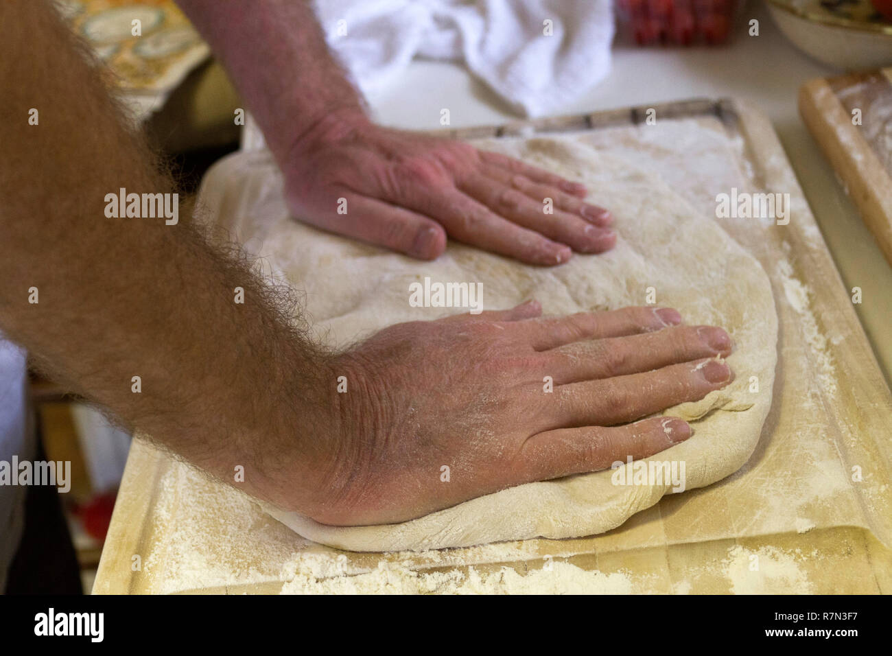 Close up di un uomo con le mani in mano impastare la pasta su un tagliere per rendere il pane fresco Foto Stock