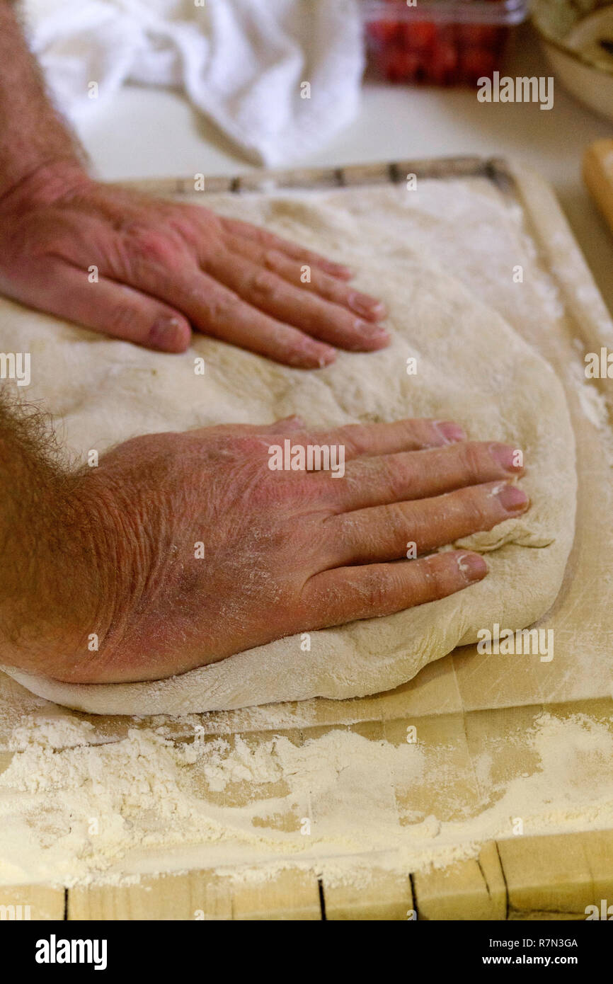 Close up di un uomo con le mani in mano impastare la pasta su un tagliere per rendere il pane fresco Foto Stock
