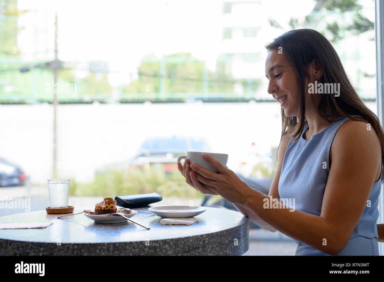 Vista di profilo di giovane imprenditrice felice di bere il caffè mediante la finestra Foto Stock
