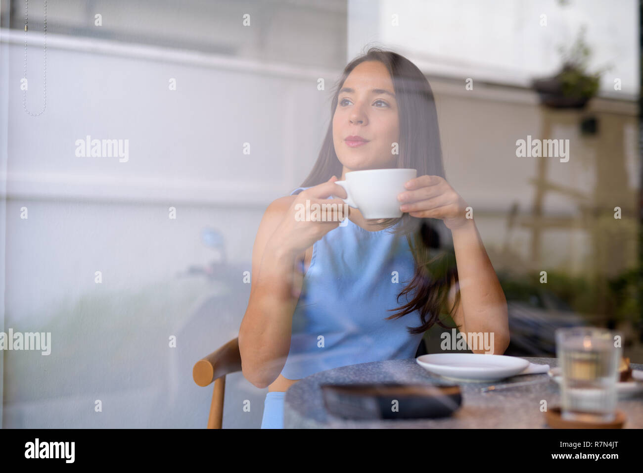 Riflessivo giovane imprenditrice di bere il caffè guardando attraverso la finestra Foto Stock
