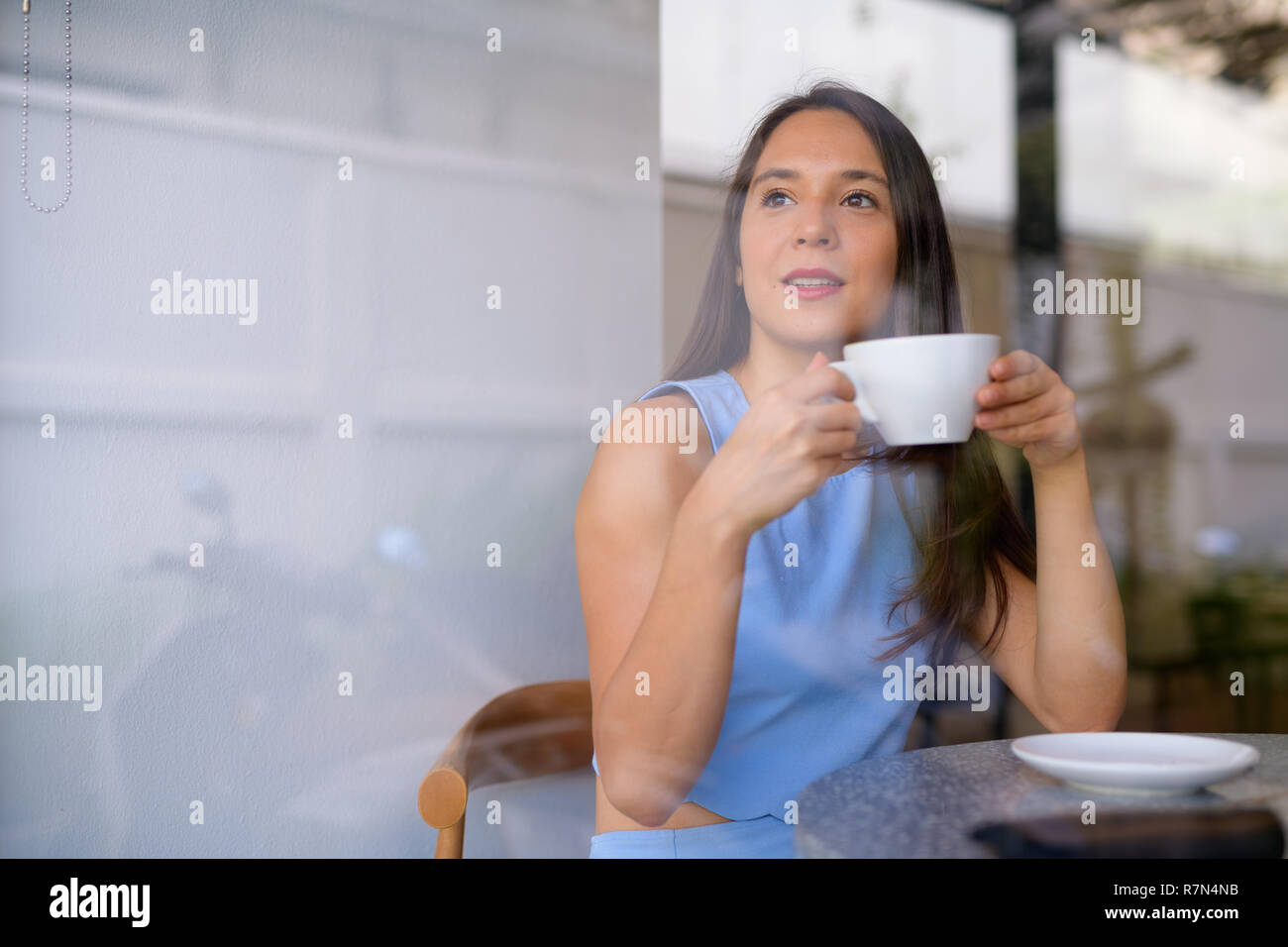 Riflessivo giovane imprenditrice di bere il caffè guardando attraverso la finestra presso il cafe Foto Stock