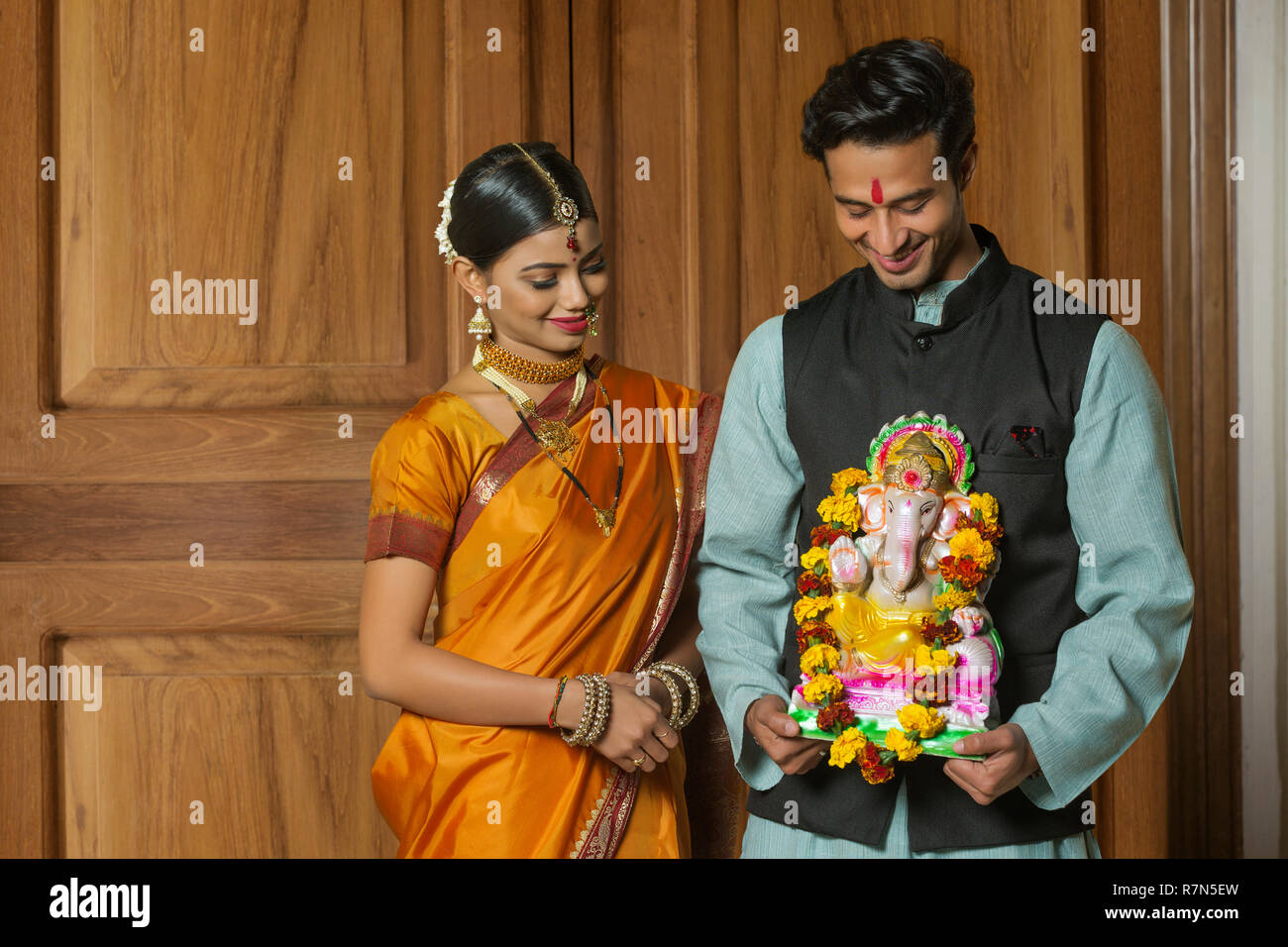 Maharashtrian giovane in abito tradizionale celebrando ganapati festival tenendo una piccola statua del signore ganesha e lo sta guardando. Foto Stock