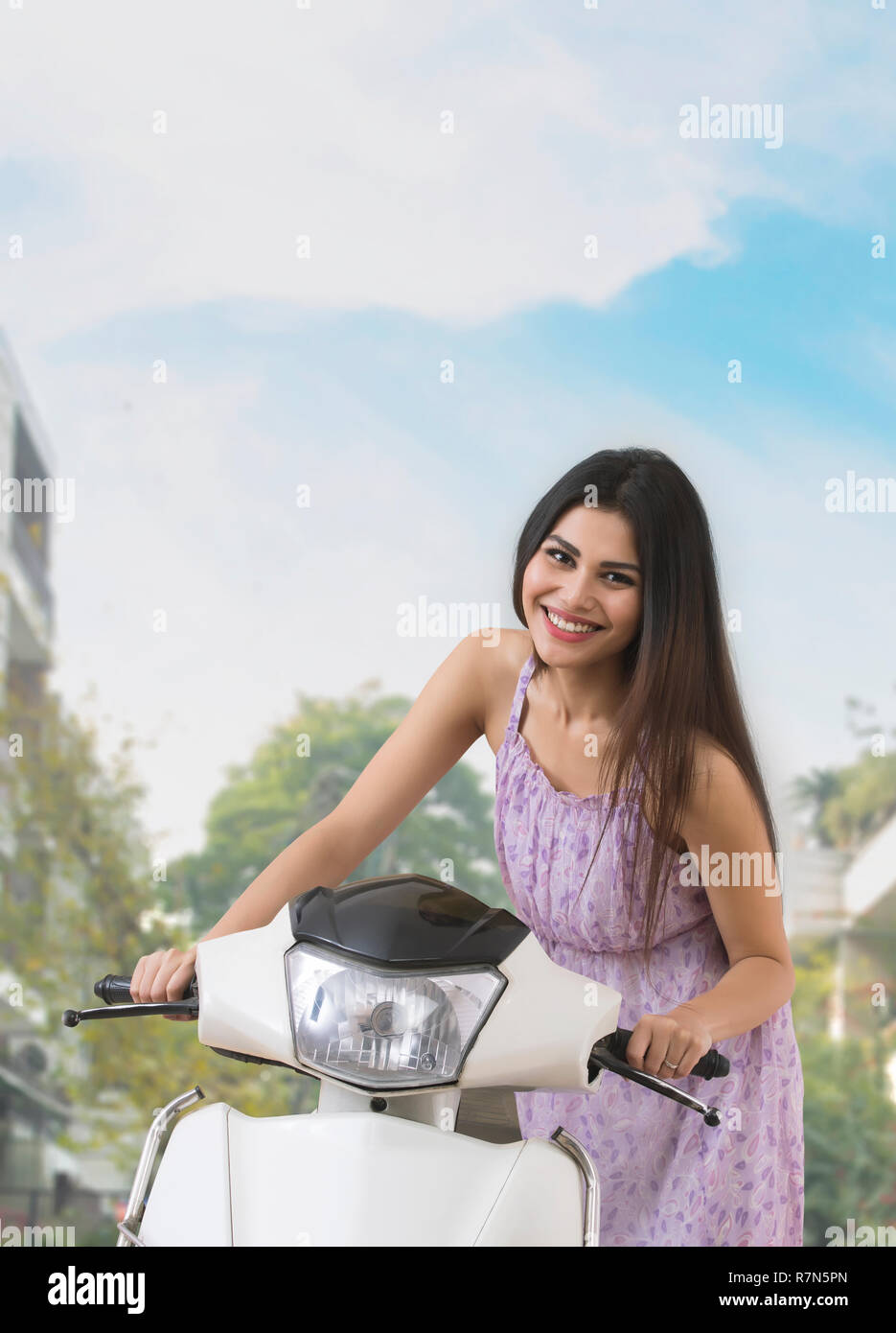 Ritratto di un sorridente giovane donna in posa con uno scooter all'esterno. Foto Stock