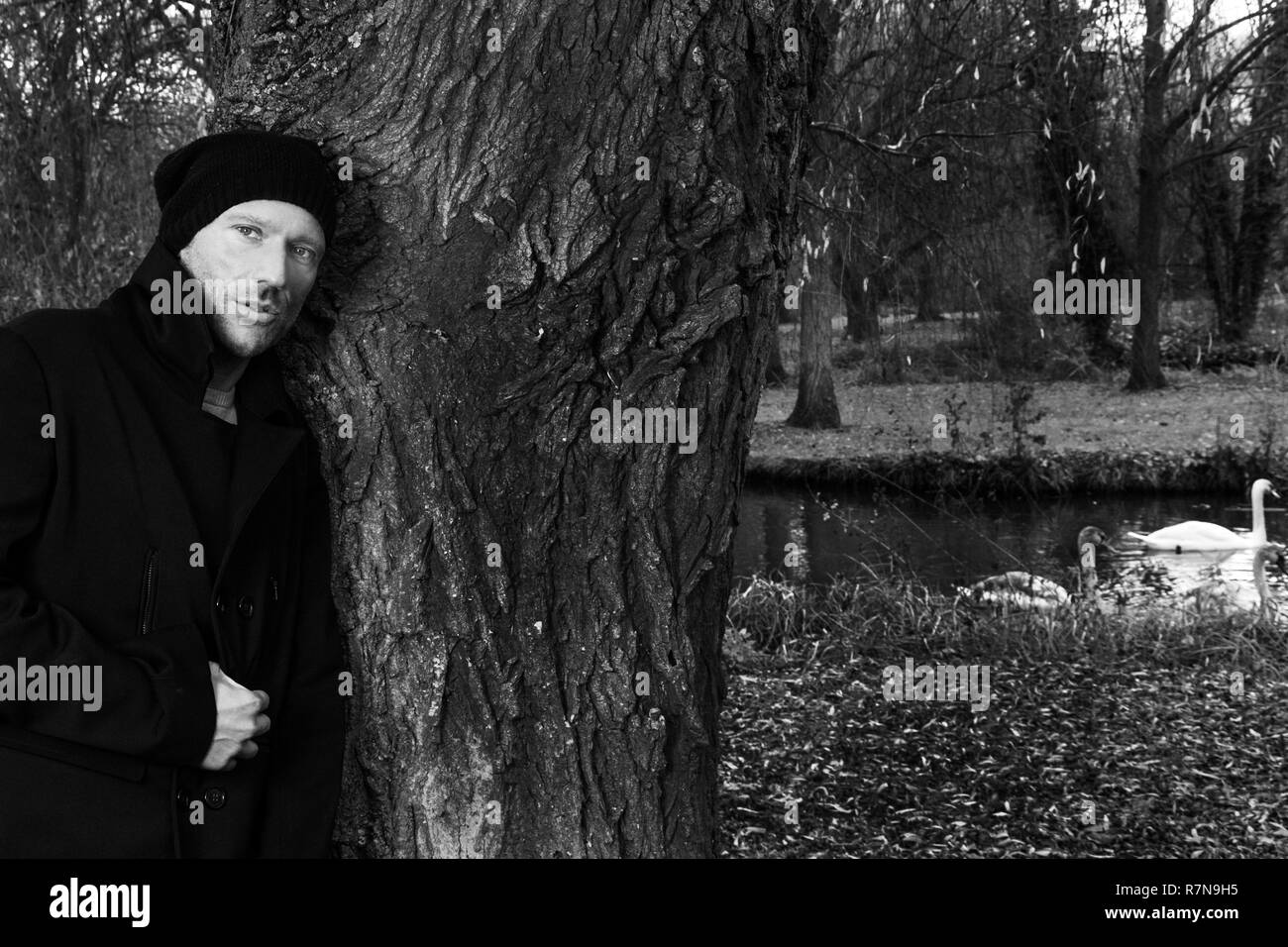 Bianco e nero ritratto di uomo bello appoggiato contro l'albero nel parco con il lago dei cigni e in background Foto Stock