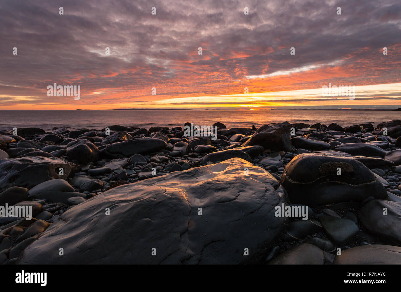 Sunset Over Mull of Galloway da un bouldery Beach sulla costa Machars nel sud-ovest della Scozia. Foto Stock