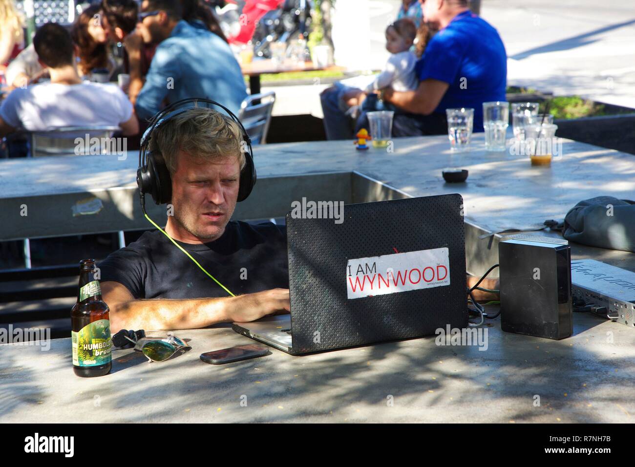 Stati Uniti, Florida, Miami, Geek collegato al suo computer portatile sulla terrazza di un caffè alla moda, nel distretto di Wynwood Foto Stock
