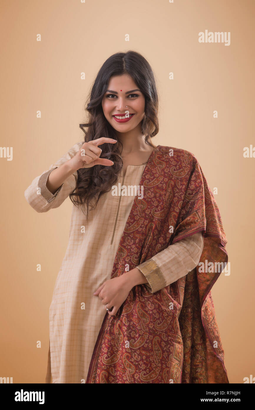 Ritratto di un sorridente giovane donna in abito tradizionale mantenendo le dita come in possesso di un prodotto. Foto Stock