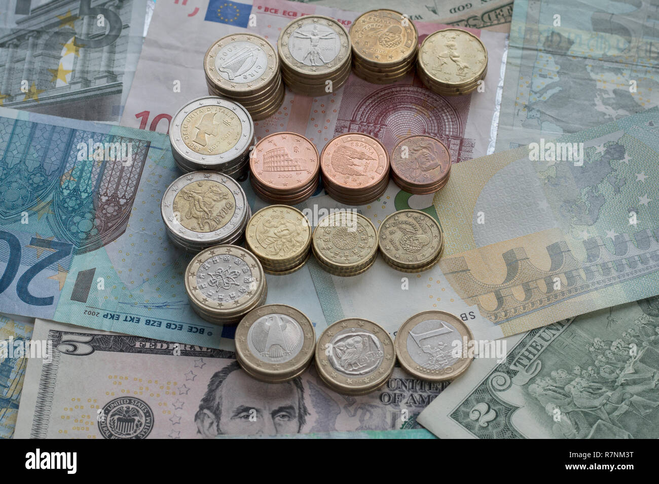 Pile di monete metalliche in euro nella forma di un simbolo dell'euro. Sfondo di banconote. Euro e Dollari USA valuta. Messa a fuoco selettiva. Foto Stock