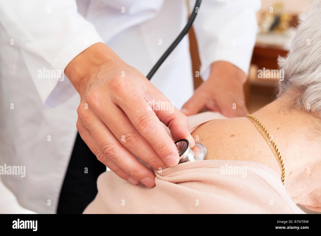 Primo piano di un medico caucasica uomo in camice bianco, auscultating senior caucasica donna paziente utilizzando uno stetoscopio, a casa sua o ad una assistenza infermieristica hom Foto Stock
