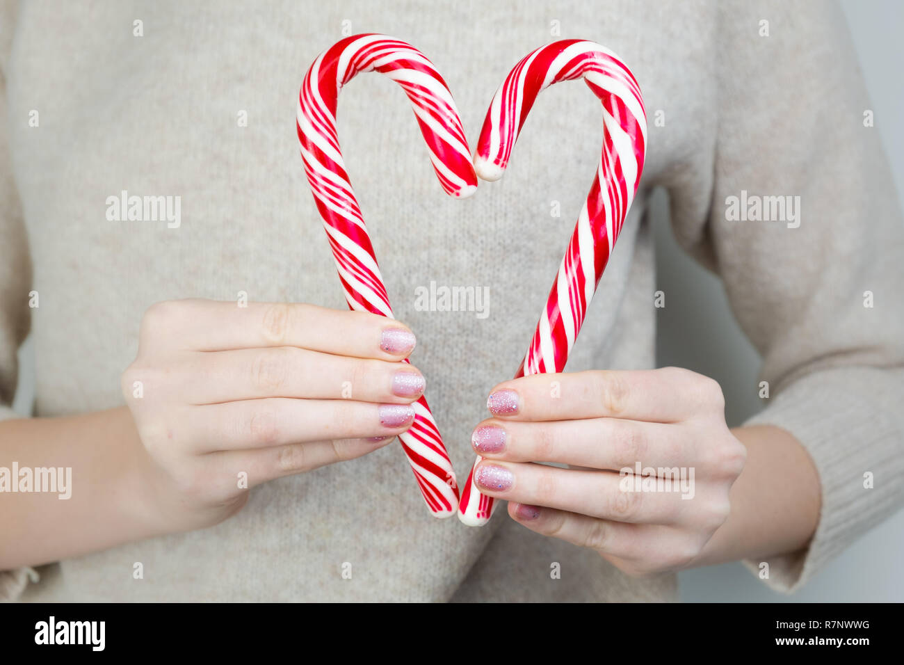 Forma di cuore fatta di due canne di caramella. Concetto di carità: femmina trattiene due caramelle cuore di formazione a livello del petto. Foto Stock