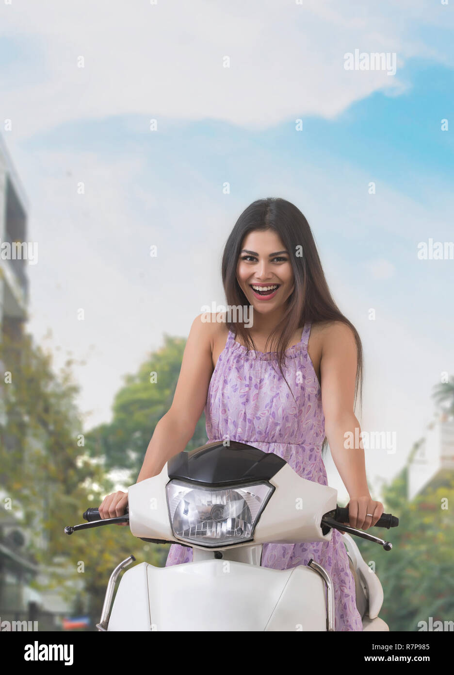 Ritratto di un sorridente giovane donna seduta su di uno scooter all'esterno. Foto Stock