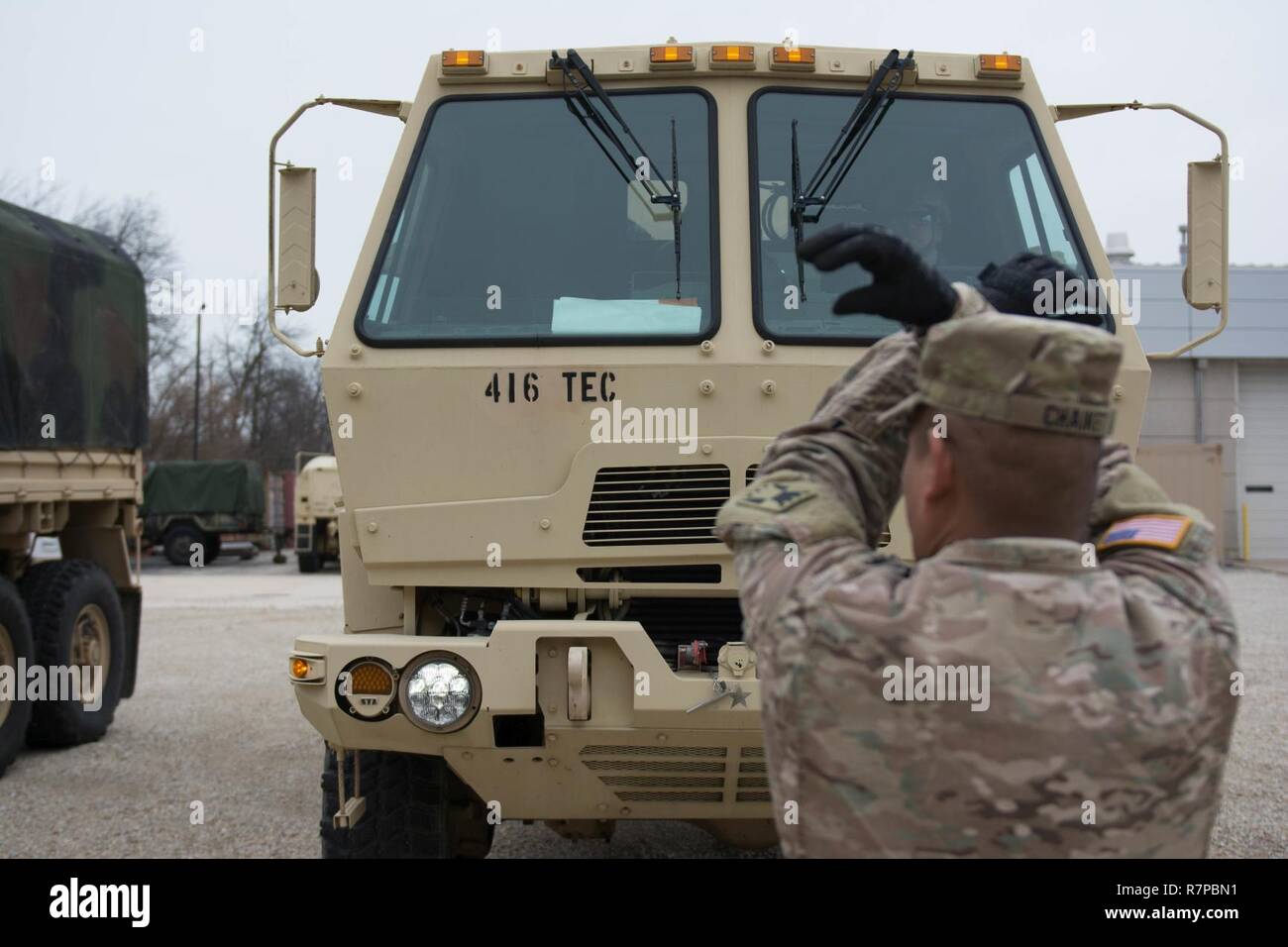 Un soldato con HHC 416th TEC utilizza la mano e il braccio segnali alla guida di massa un M1083 A1 medie veicolo tattico per un arresto. Massa di procedure di guida in un area congestionata sono di vitale importanza per la sicurezza militare. Massa di procedure di guida erano parte del curriculum insegnate durante HHC week-long conducente corso di formazione Foto Stock