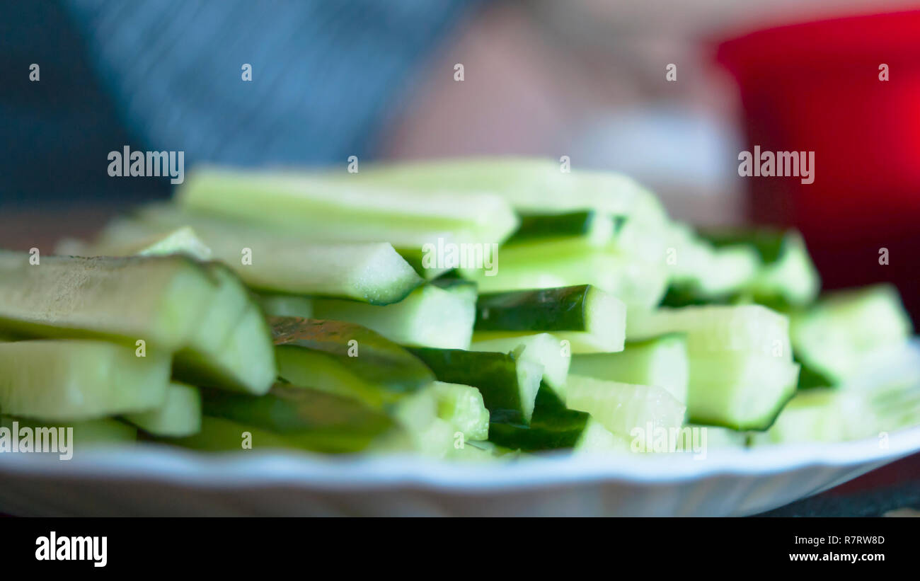 Tagliare il cetriolo bastoni su una piastra bianca. Può essere usato per fare insalate o Hosomaki, cetriolo Sushi rotoli, o Kappa Maki. Cucina sfocata sullo sfondo. Foto Stock