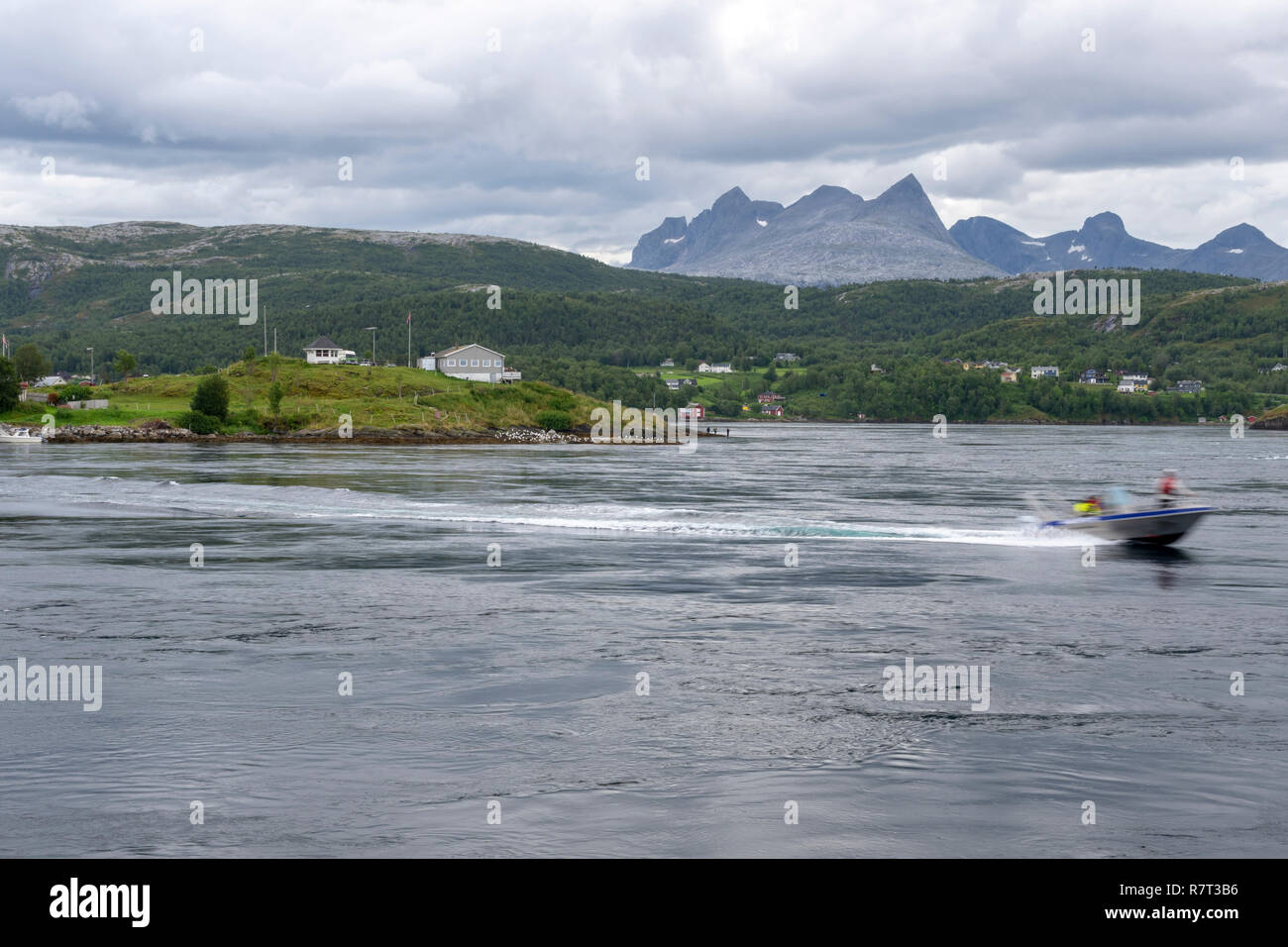 Barca da pesca a guidare la aganist Saltstraumen corrente di marea uno del più forte corrente di marea nel mondo con Børvasstindene montagne e cloud Foto Stock