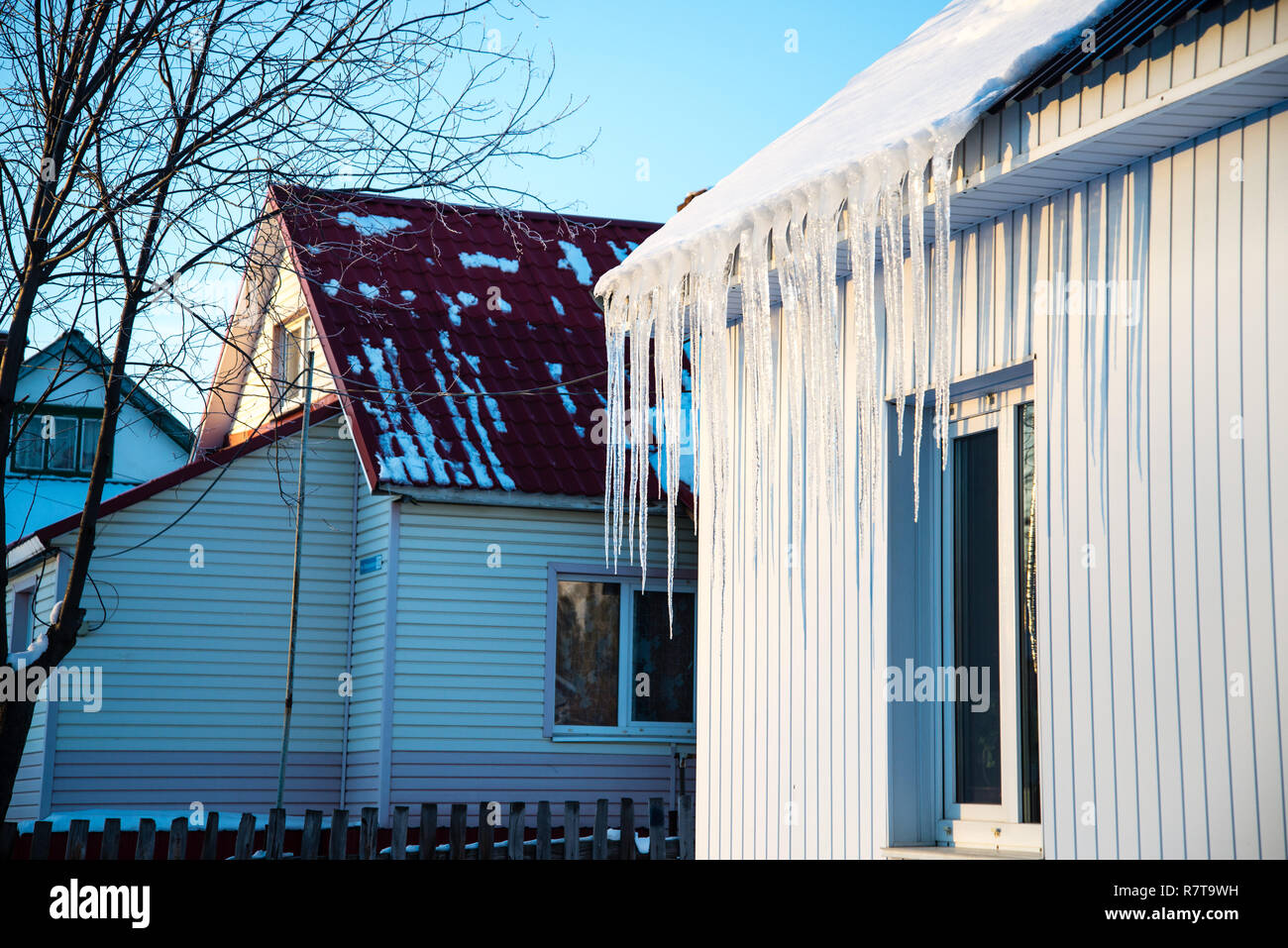 La piccola casa con ghiaccioli. Edilizia residenziale in una giornata invernale, un po' di neve sul tetto al sole, inquadratura orizzontale Foto Stock