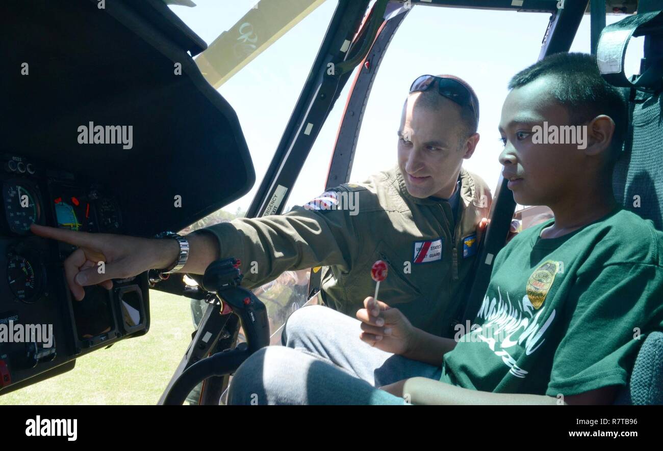 Lt. Ryan Popiel, un MH-65 Delfino pilota di elicottero dalla guardia costiera Stazione aria Barbieri punto, Oahu, spiega elicottero strumenti per uno studente come parte di un evento D.A.R.E. per Kualapuu carta pubblica la scuola dei bambini a Kaunakakai Ball Park, Molokai, Aprile 7, 2016. Il rally si è tenuta a informare i bambini sui pericoli della droga e comprendeva anche dimostrazioni da parte della guardia costiera Stazione aria Barbieri punto, Guardia nazionale, Maui il dipartimento di polizia della contea di Maui Vigili del Fuoco, Hawaii Dipartimento della Terra e delle risorse naturali e numerose altre agenzie. Foto Stock