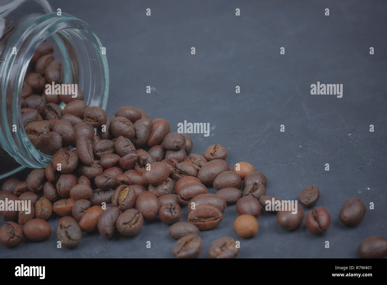 Chicchi di caffè tostati versata da un vasetto di vetro. il posizionamento angolare del caffè in oggetto. Foto Stock