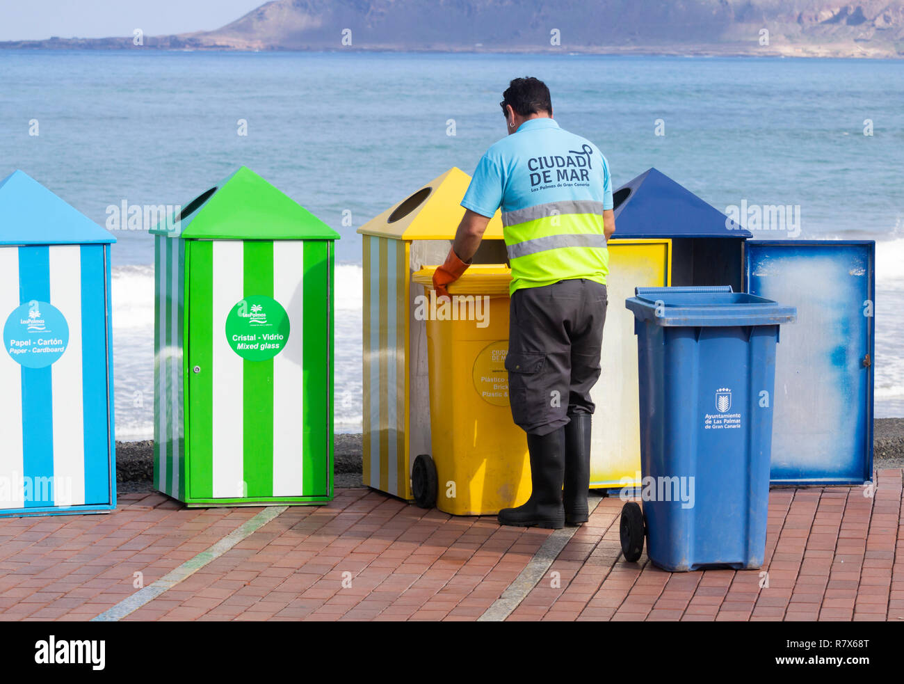 Consiglio lo svuotamento del lavoratore con codice colore di cassonetti per il riciclaggio della plastica, della carta, organico...sulla spiaggia in Spagna Foto Stock