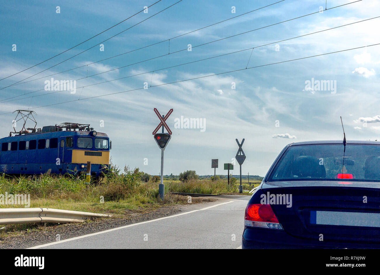 Il treno elettrico avvicinamento attraversamento ferroviario. Auto in piedi davanti la stazione di incrocio con semaforo e cartello stradale senza una barriera Foto Stock