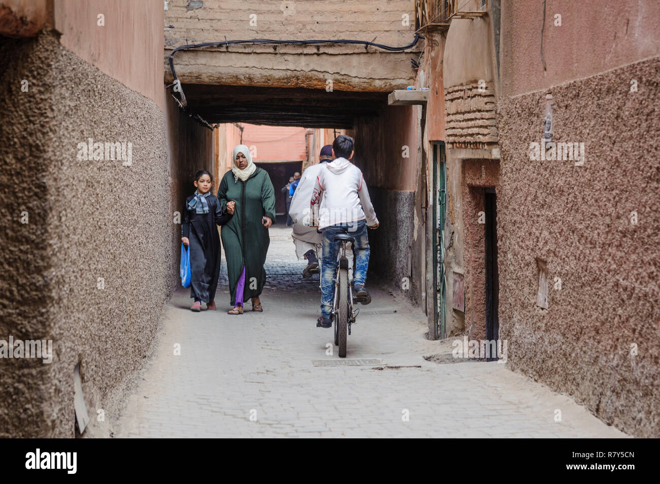 05-03-15, Marrakech, Marocco. Scena di strada nel souk della medina, nella vecchia, antico, parte della citta'. Ragazzi su biciclette passano una madre e daugh Foto Stock