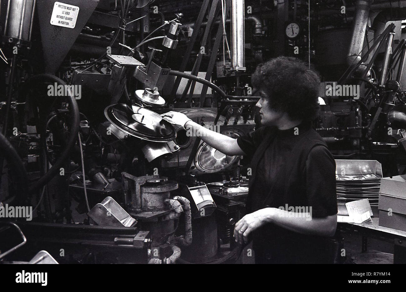 Anni Settanta, storico, il lavoratore di sesso femminile in un impianto di produzione utilizzando un macchinario per lo stampaggio di dischi in vinile, STATI UNITI D'AMERICA. Foto Stock