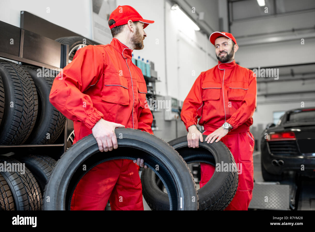 Servizio auto di lavoratori in rosso uniforme che porta nuovi pneumatici al montaggio del pneumatico o il servizio shop Foto Stock