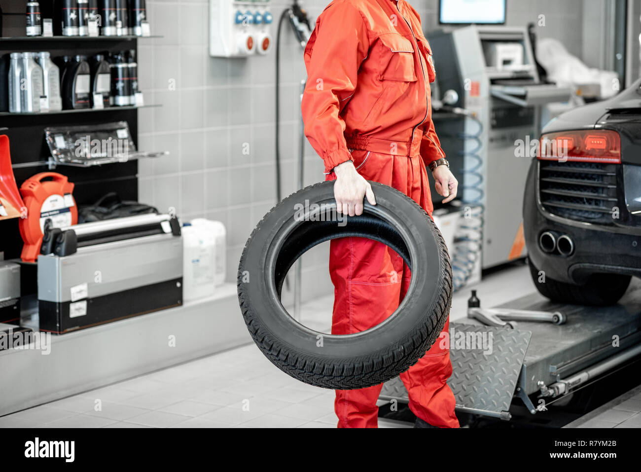 Auto di servizio lavoratore in rosso uniforme che porta nuovi pneumatici al montaggio del pneumatico o il servizio shop Foto Stock