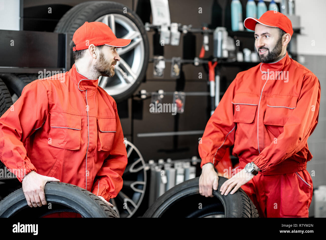 Servizio auto di lavoratori in rosso uniforme che porta nuovi pneumatici al montaggio del pneumatico o il servizio shop Foto Stock