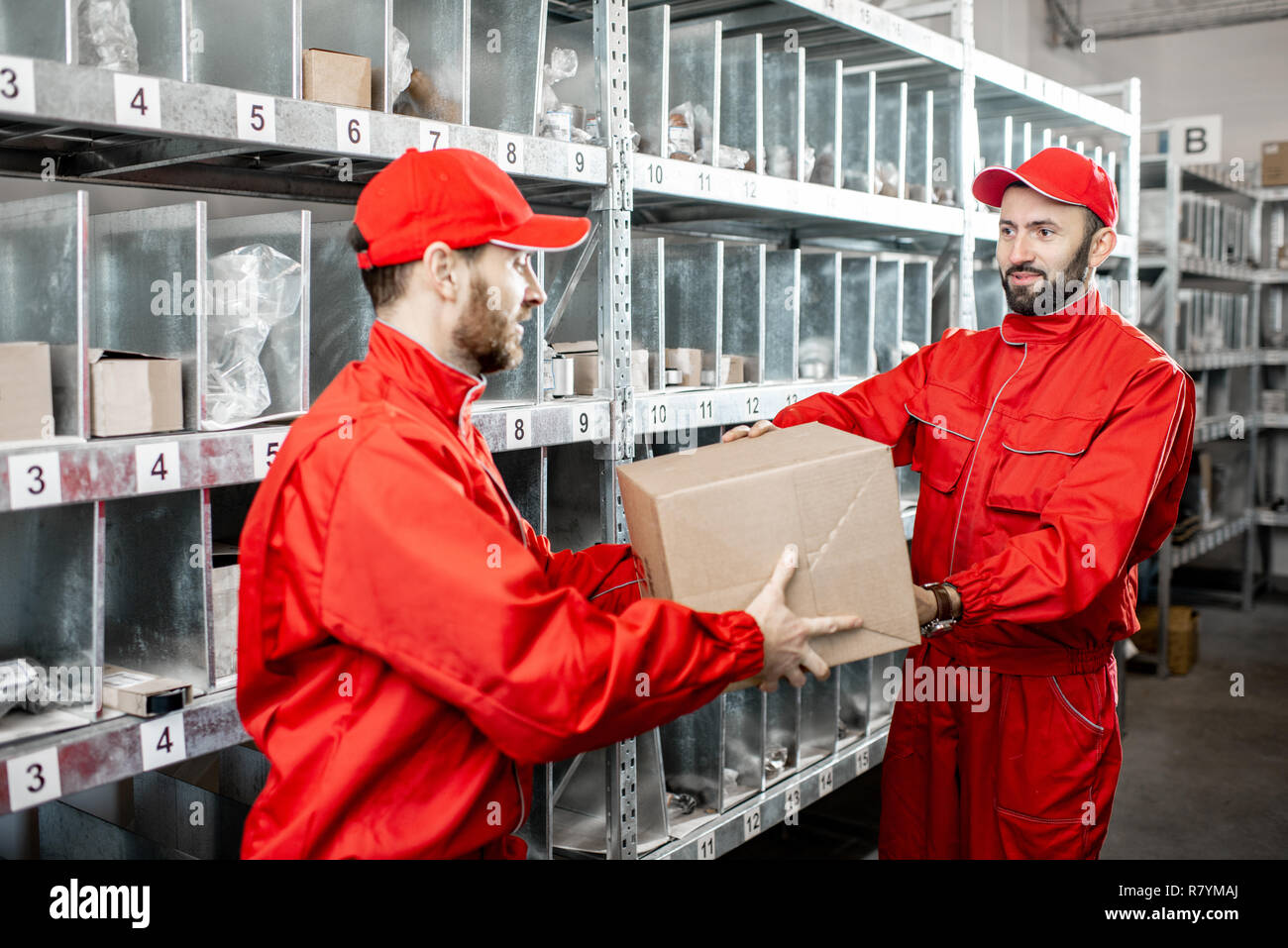 Due bello magazzinieri in rosso uniforme con permanente di caselle in storage con ricambi auto o altri prodotti Foto Stock