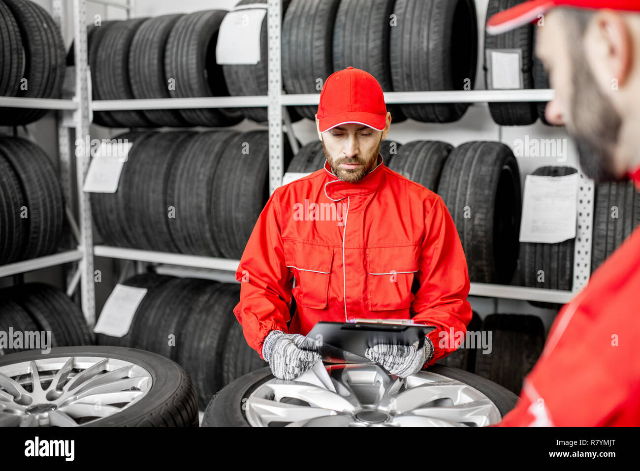 Lavoratore o venditore in rosso uniforme riempimento alcuni documenti di controllo sulle merci in magazzino con pneumatici per auto Foto Stock