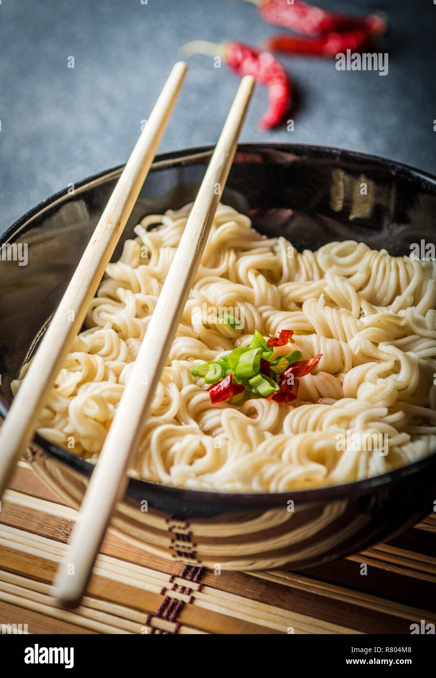 Ciotola nero di asian spaghetti istantanei con acqua calda e il peperoncino rosso e il cipollotto e bastoncini Foto Stock