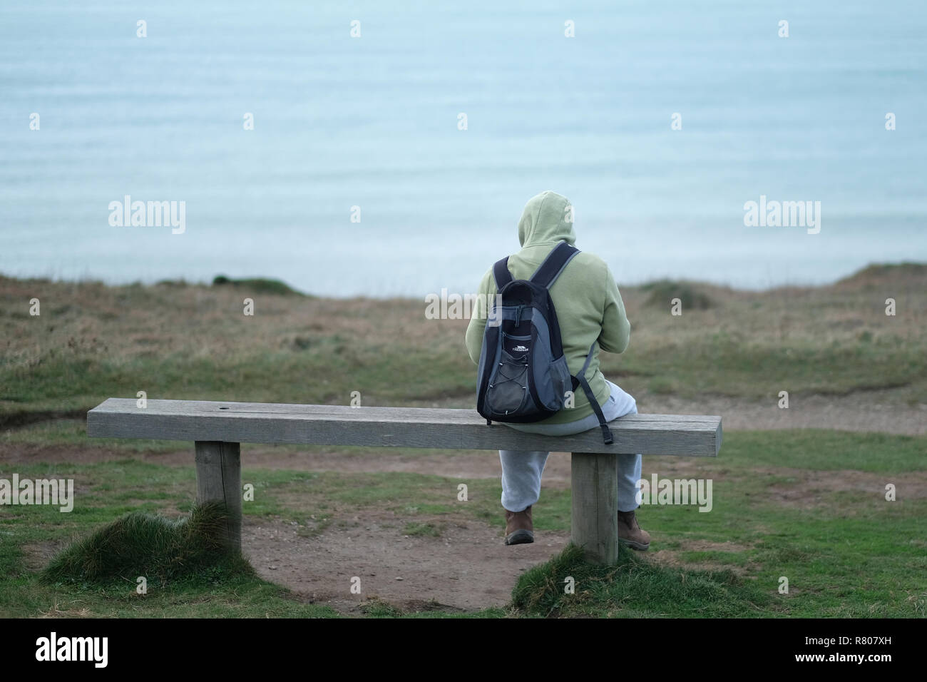 Una figura seduta su una panchina affacciata sul mare in Porthtowan, ​Cornwall, UK. Foto Stock