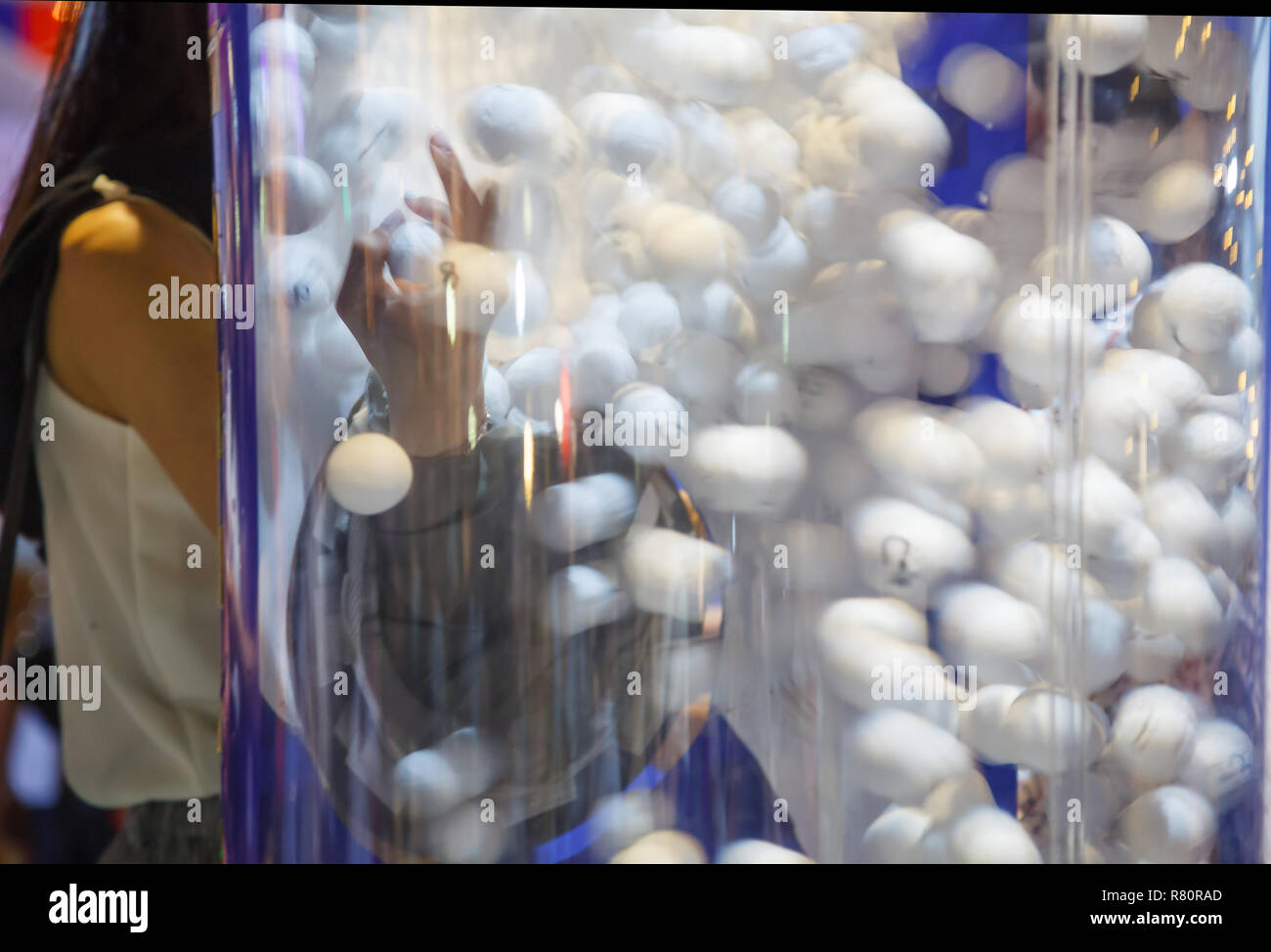 Donna mano seleziona bianco palline da ping pong fortunato trarre in aria macchina lotteria lotteria (disegno a sfera o sfera di bingo macchina soffiante) nella carità evento. Il gioco d'azzardo Foto Stock