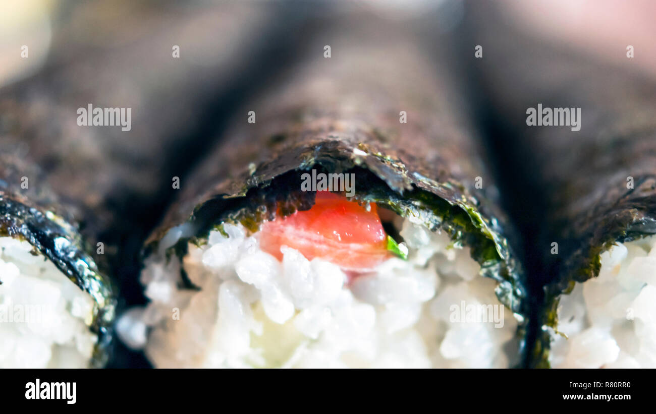 Immagine dettagliata dei rotoli di Sushi con Nori alghe, Rosso di pesce e riso per la tenuta sul bordo prima di affettatura. Foto Stock