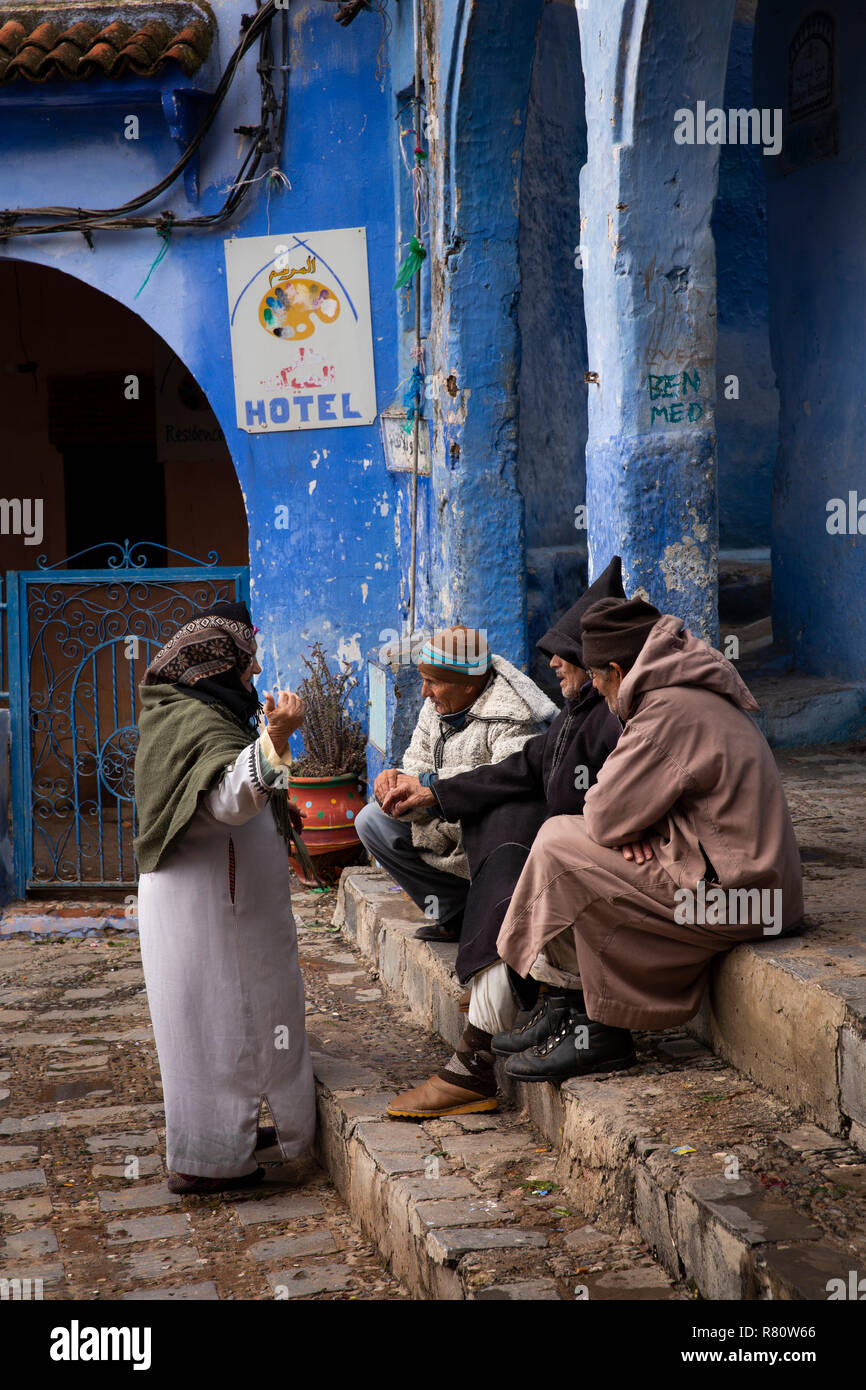Il Marocco, Chefchaouen, città blu, luogo el Mazjen, uomini anziani in djellabas sat parlando di donna locale Foto Stock