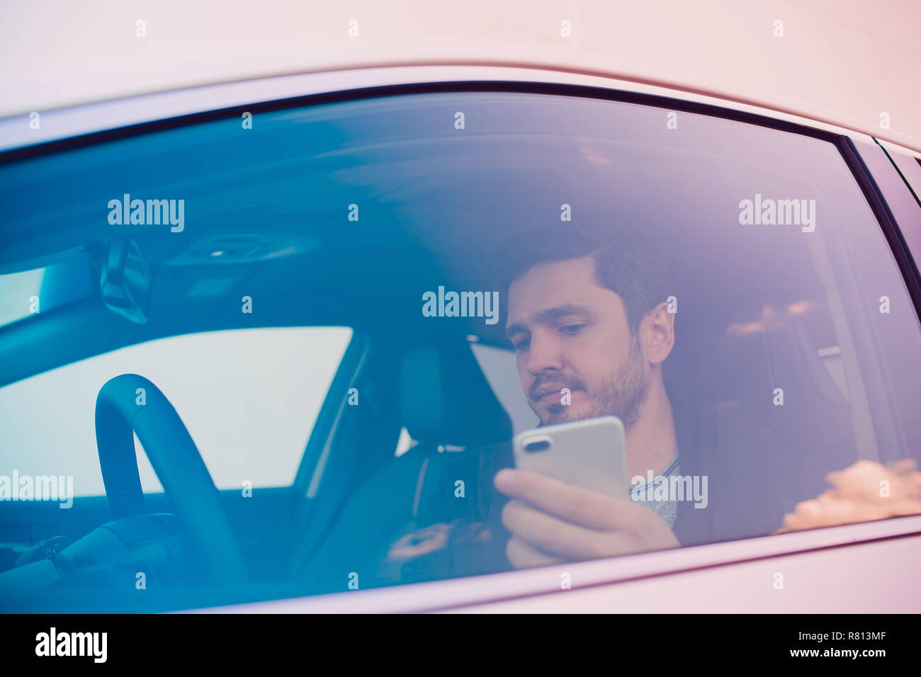 Inquadratura di un uomo bello utilizzando il telefono cellulare durante la guida. Foto Stock