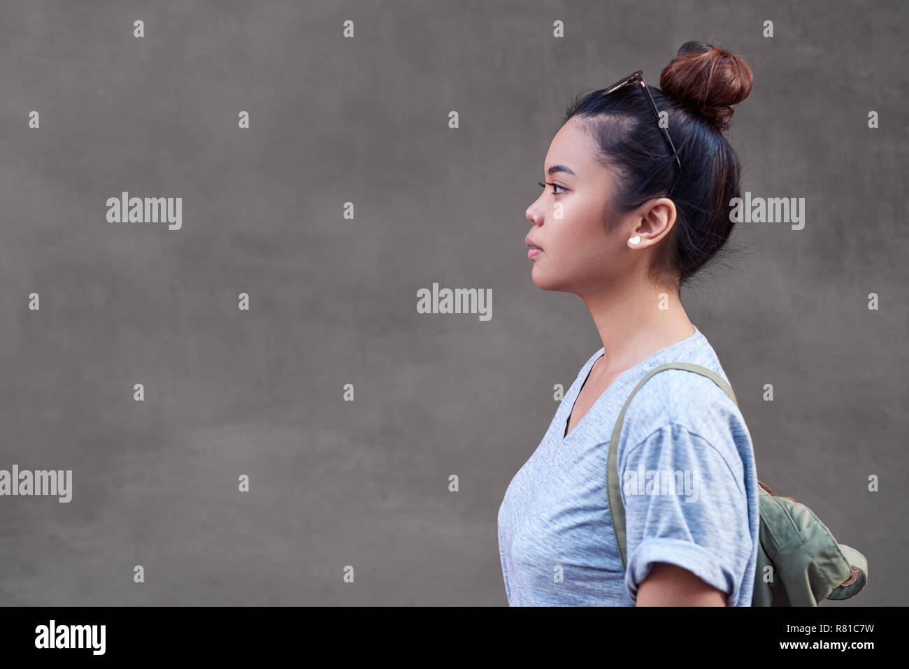 Donna asiatica lateralmente in piedi di fronte a una parete Foto Stock