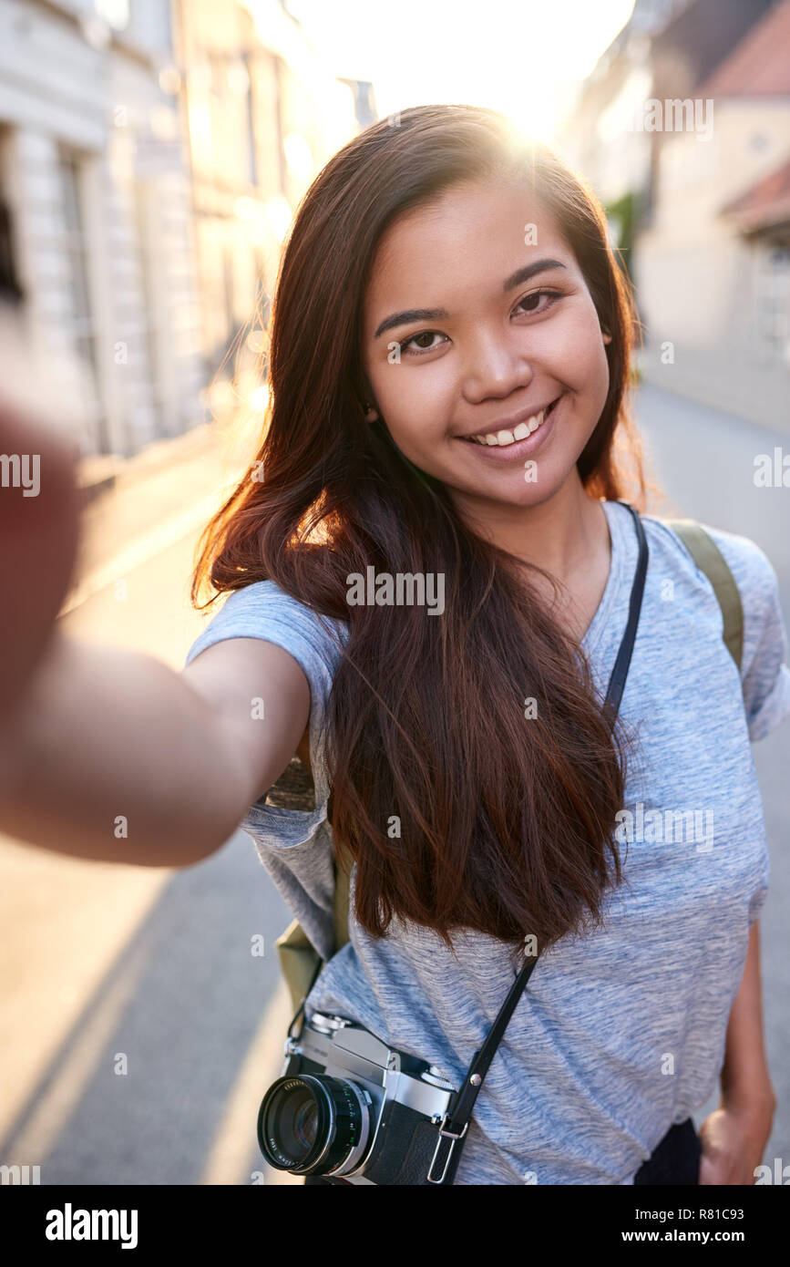 Sorridente giovane donna asiatica a piedi nella città prendendo selfies Foto Stock