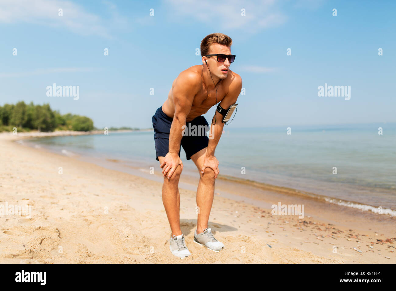 Runner maschio con auricolari e fascia per il braccio sulla spiaggia Foto Stock