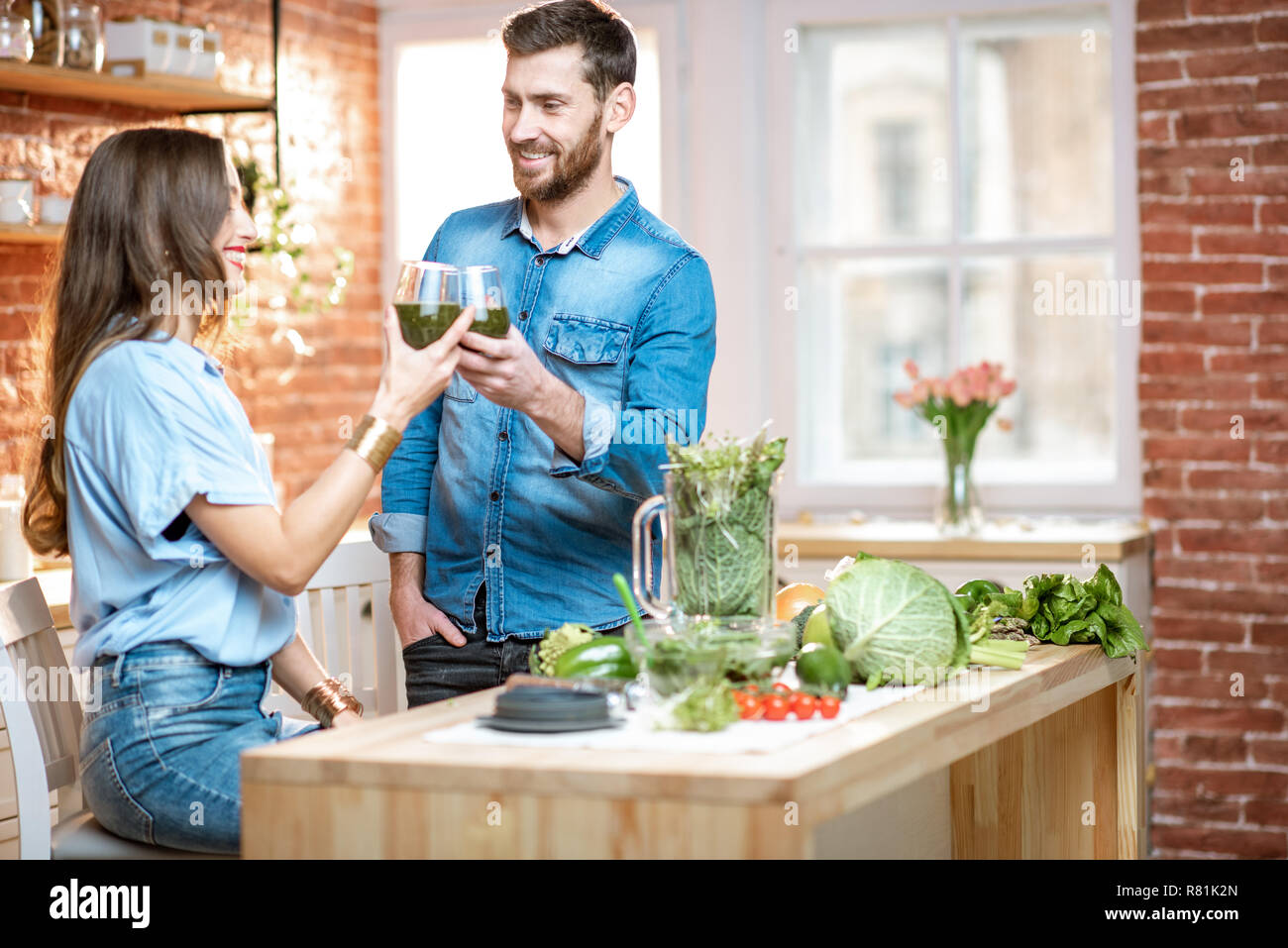 Coppia giovane di vegetariani bere frullato fresco su la cucina con il verde il cibo sano a casa Foto Stock