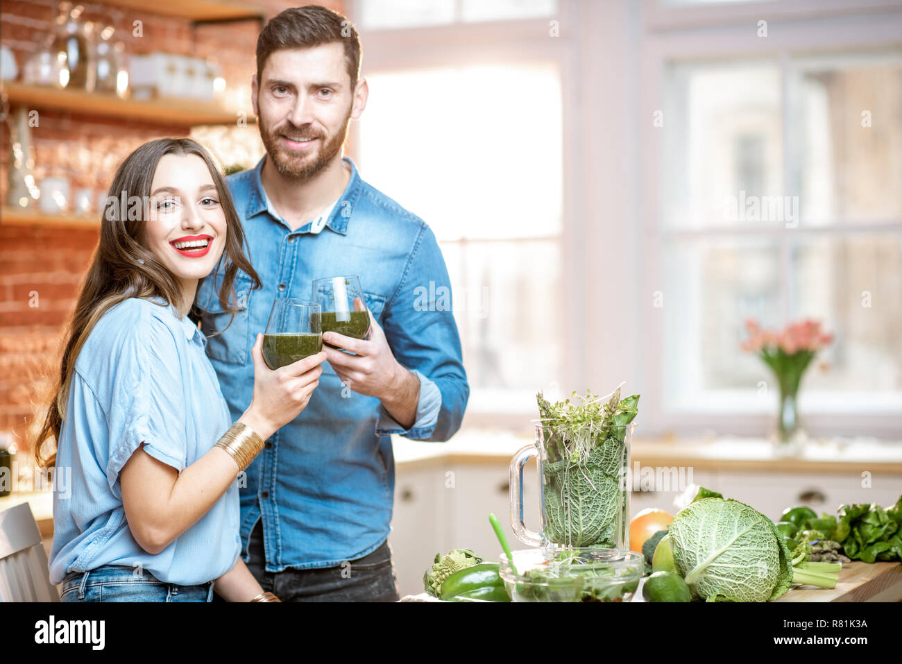 Ritratto di una giovane coppia di vegetariani bere frullato fresco su la cucina con il verde il cibo sano a casa Foto Stock