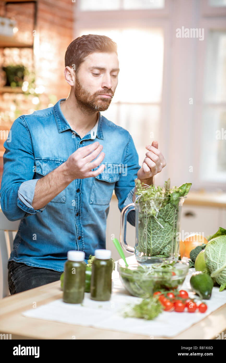 Uomo bello cercando prodotti mentre rendendo frullato vegetariano sulla cucina a casa Foto Stock