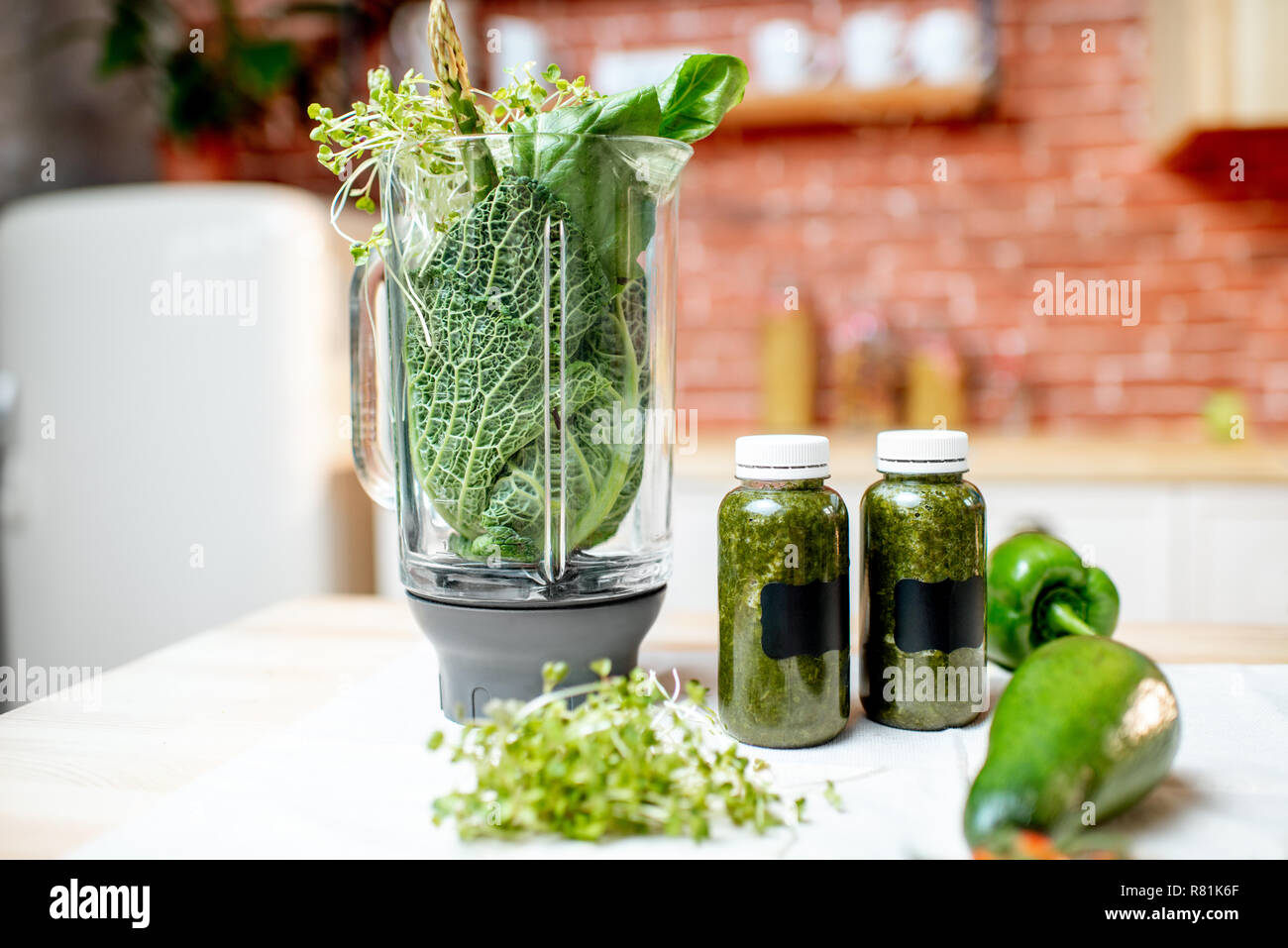 Frullatore pieno di ingredienti per rendere frullato sul tavolo verde con verdure crude in cucina Foto Stock